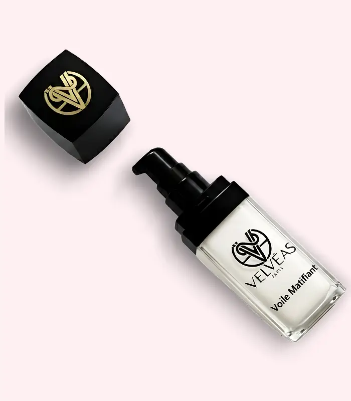 Flacon ouvert Velvéas Voile Matifiant avec pompe doseuse noire et capuchon avec logo doré posé à côté sur fond rose pâle